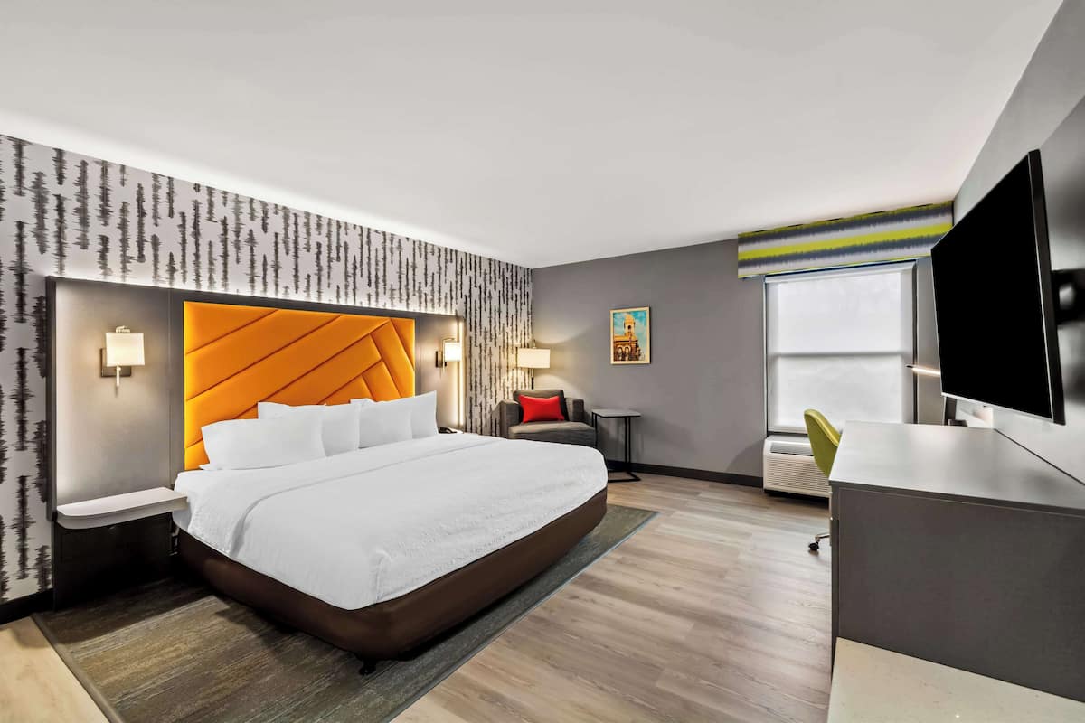 A modern hotel room with a large bed, a TV, a desk, and a window.