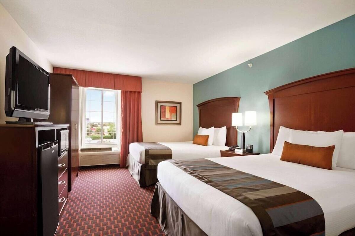 Une chambre d’hôtel avec deux lits, une télévision, un bureau et une fenêtre avec des rideaux.