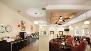 Um amplo hall de hotel com área de estar central, balcão de recepção e espaço para refeições.