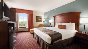 Quarto de hotel com uma cama grande, televisão, escrivaninha e janela com cortinas.
