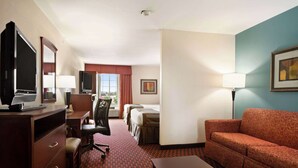 Quarto de hotel com escrivaninha, cadeira, televisão, duas camas, sofá e luminária.
