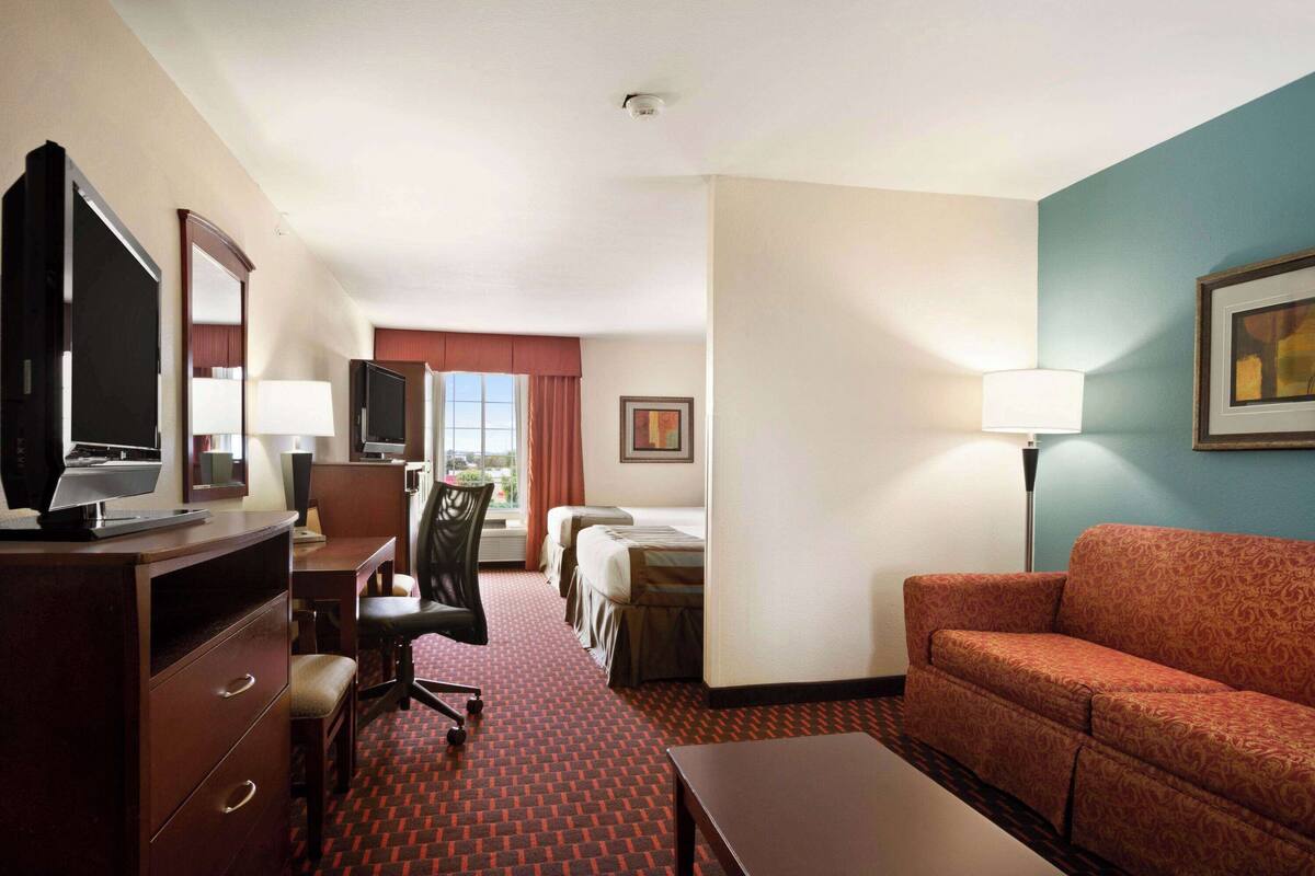 Une chambre d’hôtel équipée d’un bureau, d’une chaise, d’une télévision, de deux lits, d’un canapé et d’une lampe.
