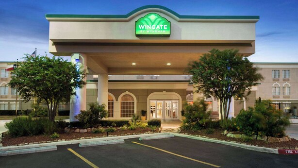 Entrada de hotel com placa verde, estacionamento e paisagismo.