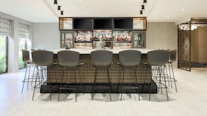 A modern bar area with a long counter, multiple chairs, and a variety of bottles and glasses. - DoubleTree by Hilton Austin - University Area (Austin)