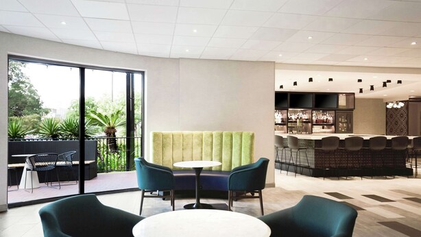 A modern indoor seating area with a bar and a view of greenery outside. - DoubleTree by Hilton Austin - University Area (Austin)
