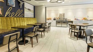A modern restaurant with a blue booth seating area, a kitchen visible in the background, and a 'hello' sign on the wall. - DoubleTree by Hilton Austin - University Area (Austin)