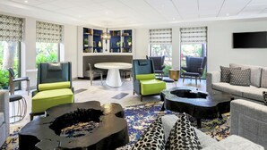 A modern living room with a round table, green and grey upholstered chairs, a sofa, and a large TV on the wall. - DoubleTree by Hilton Austin - University Area (Austin)
