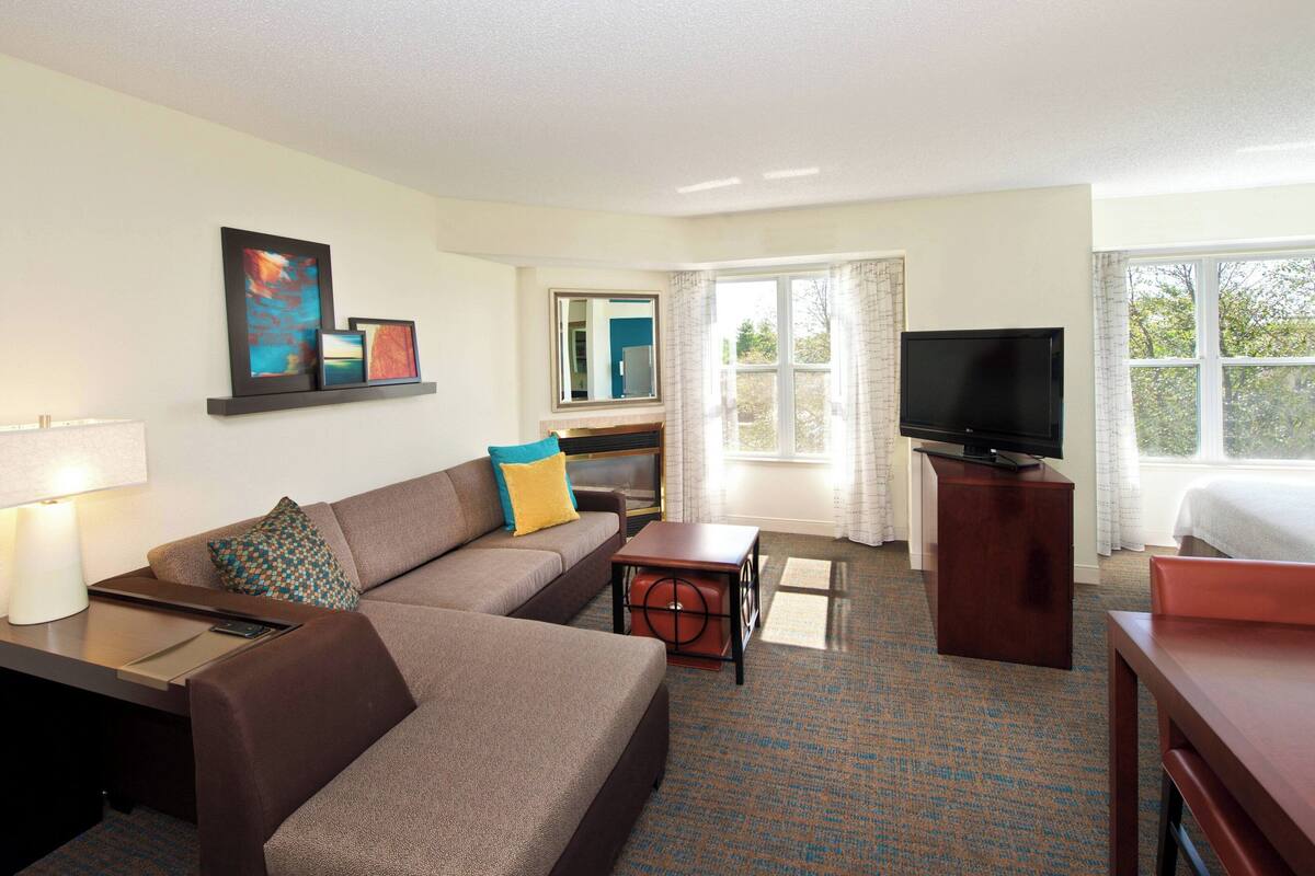 A hotel room with a sofa, a small table, a TV, and a window with curtains.