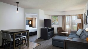 Una habitación de hotel con cama, televisión, sofá, escritorio con sillas y una mesita.