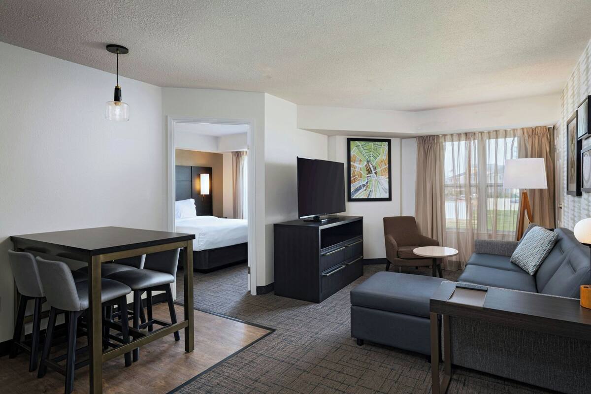 A hotel room with a bed, a TV, a sofa, a desk with chairs, and a small table.