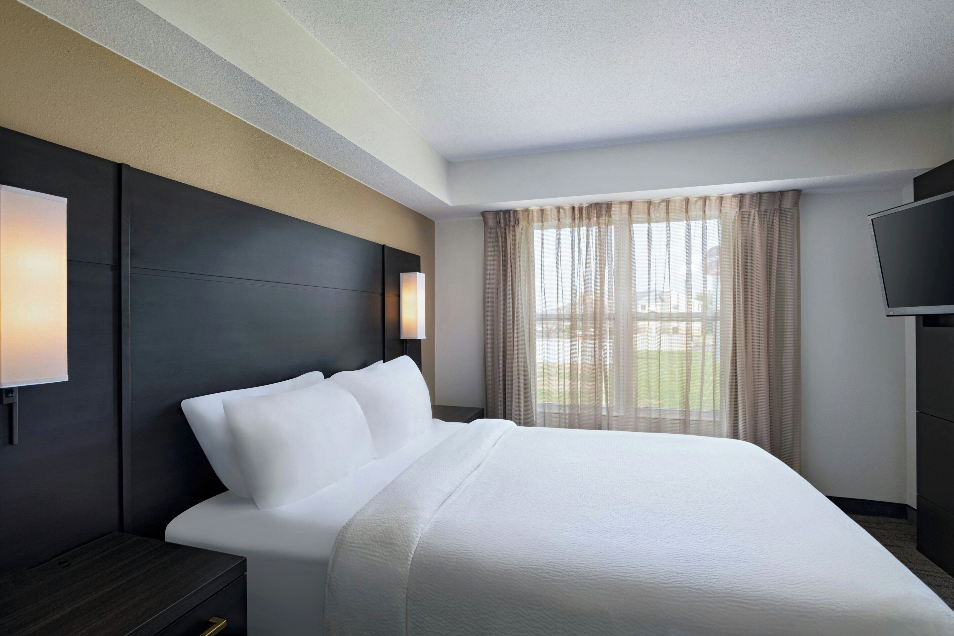 A hotel room with a bed, a TV, a nightstand, and a window with curtains.