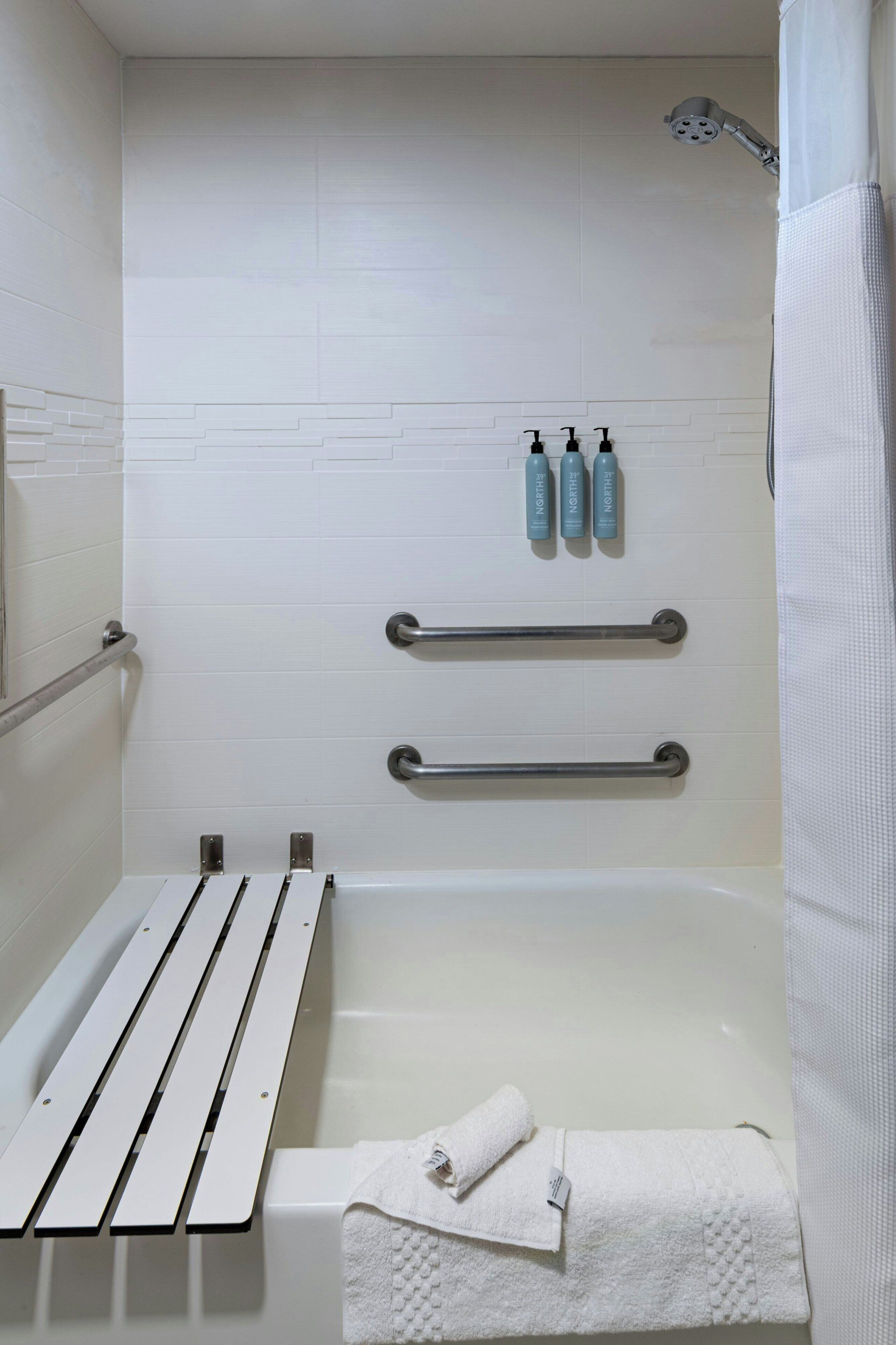 A bathroom with a bathtub, a shower, a towel rack, and three bottles of shampoo.