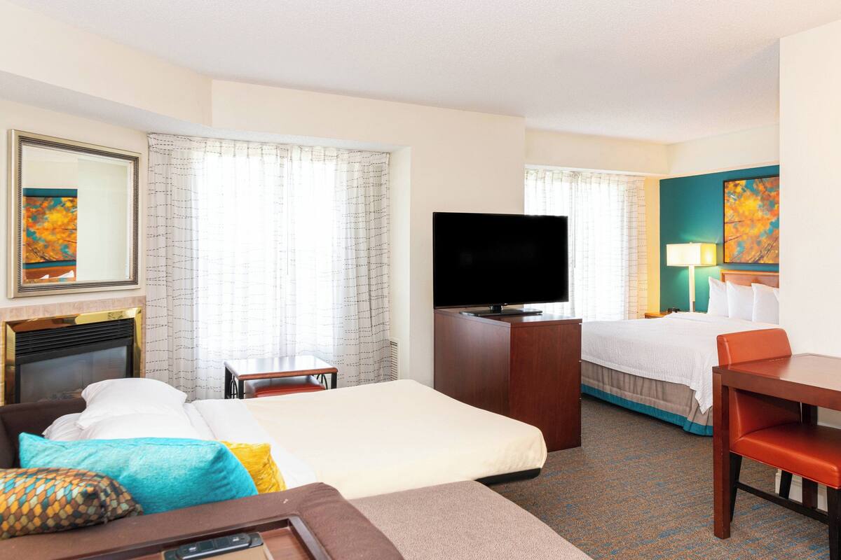 A hotel room with a bed, a desk, a television, and a fireplace.