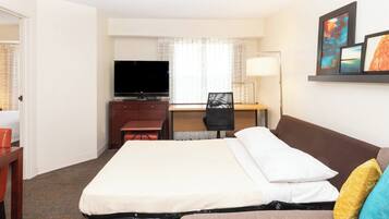 A hotel room with a bed, a desk with a chair, a television, and a window with curtains.