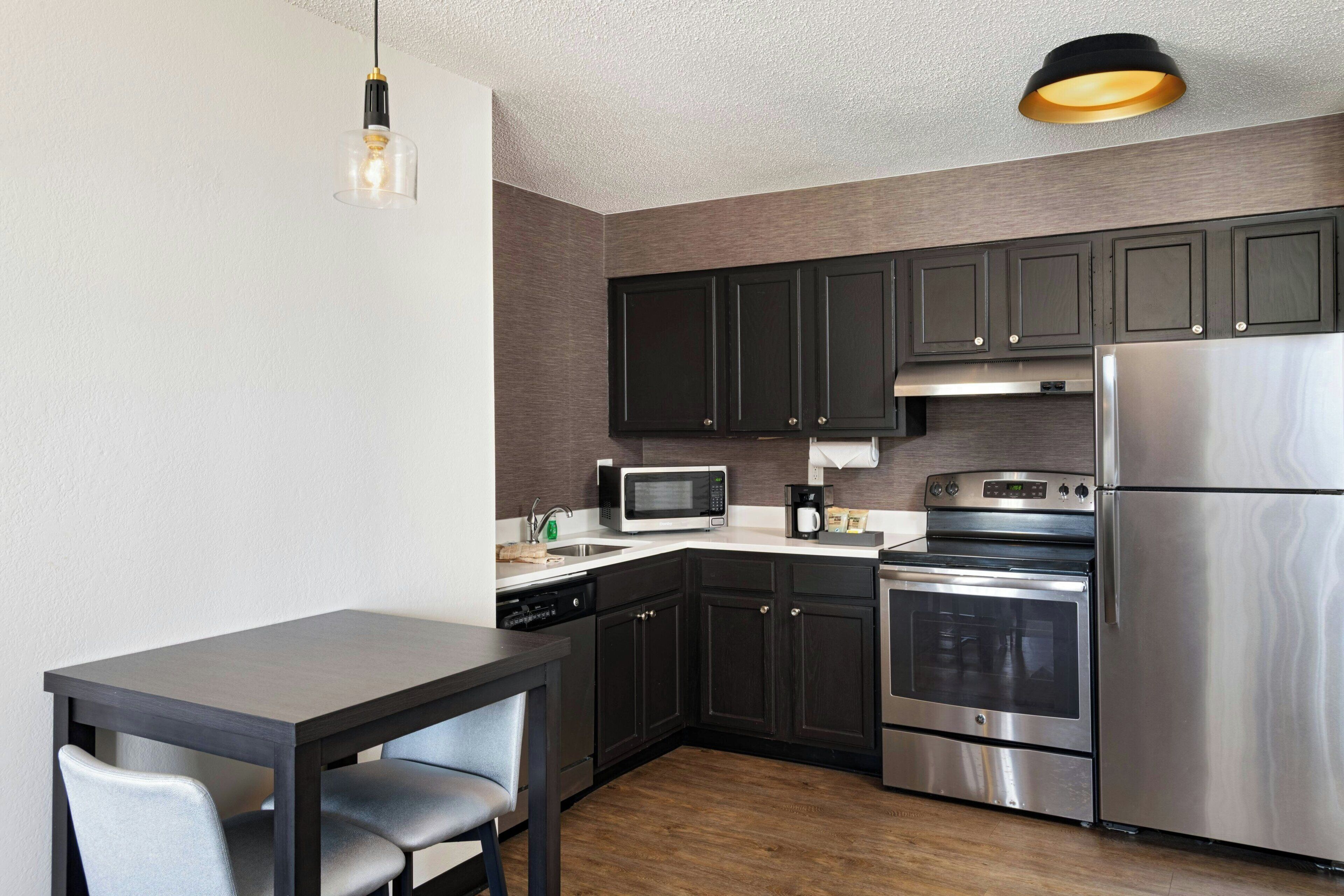 A modern kitchen with dark cabinets, stainless steel appliances, a microwave, oven, and a dining table with chairs.