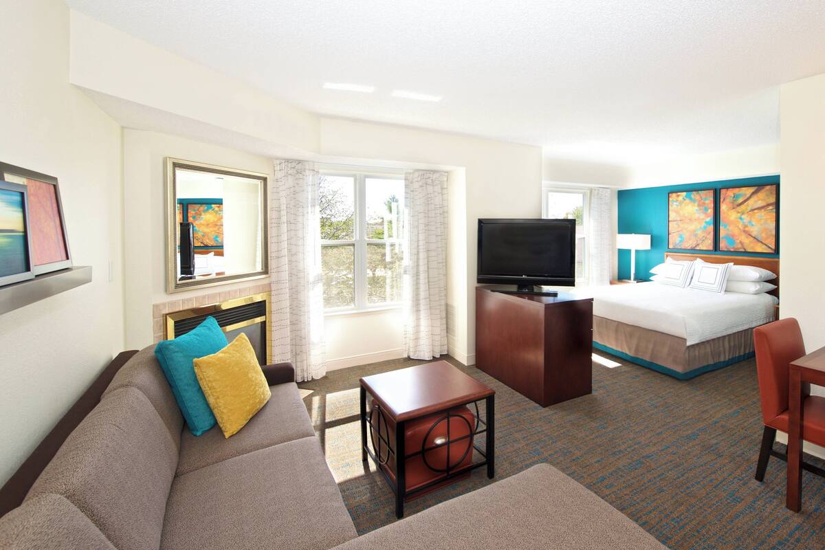 A hotel room with a sofa, a small table, a TV, a bed, and a desk.