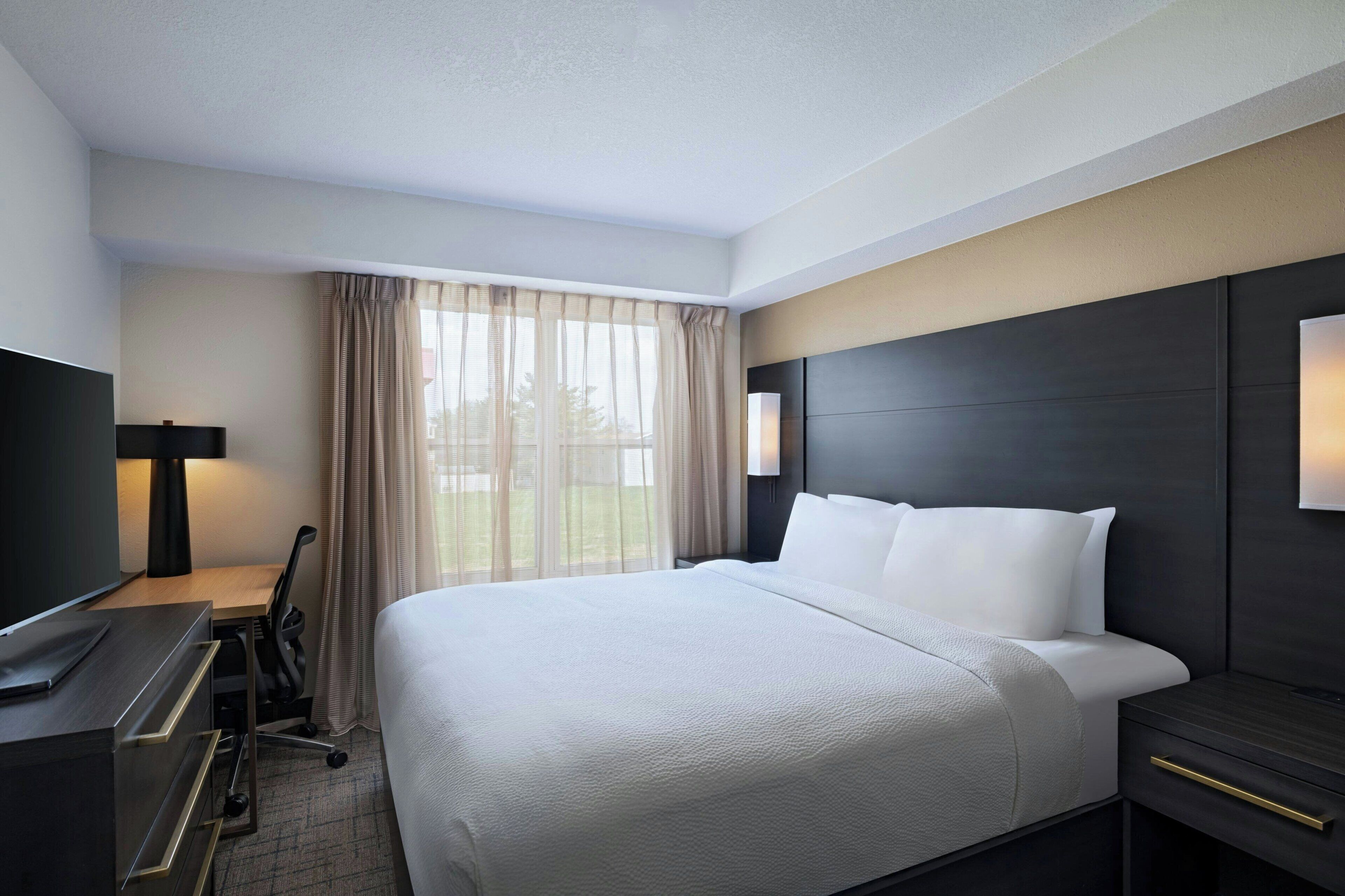 A hotel room with a large bed, a desk with a chair, a TV, and a window with curtains.