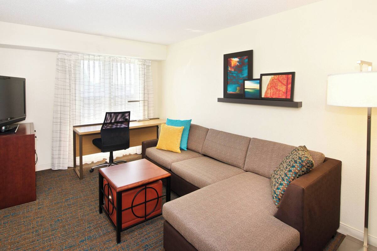A hotel room with a sofa, a desk, a television, and a lamp.