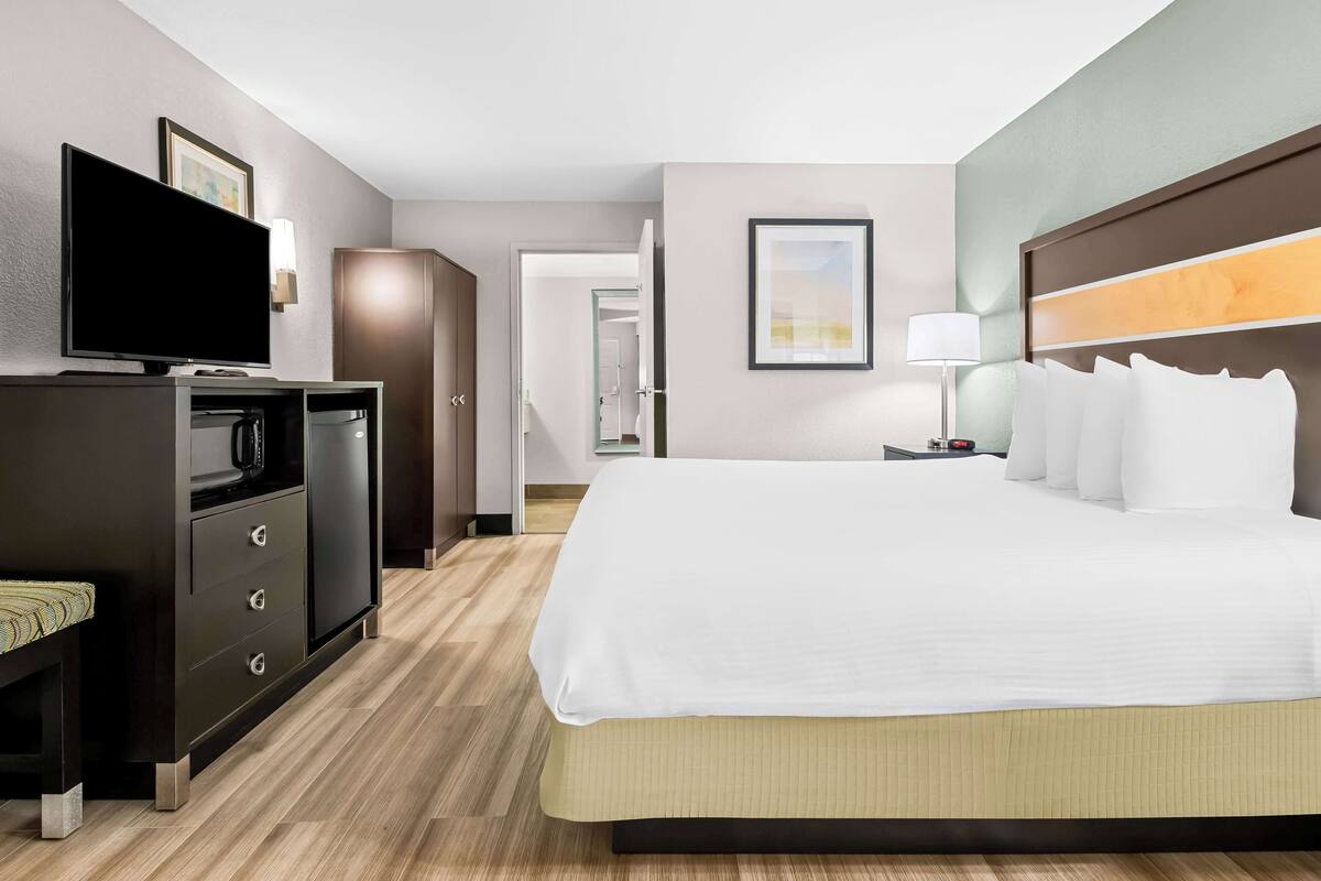 A hotel room with a large bed, a flat-screen TV, a desk with a lamp, and a wardrobe.