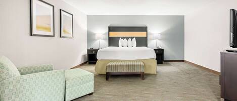 A hotel room with a bed, two bedside tables, a bench, a TV, and framed pictures on the wall.