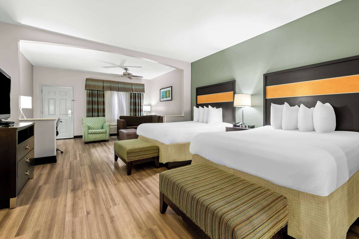 A hotel room with two beds, a desk, a chair, a TV, and a ceiling fan.