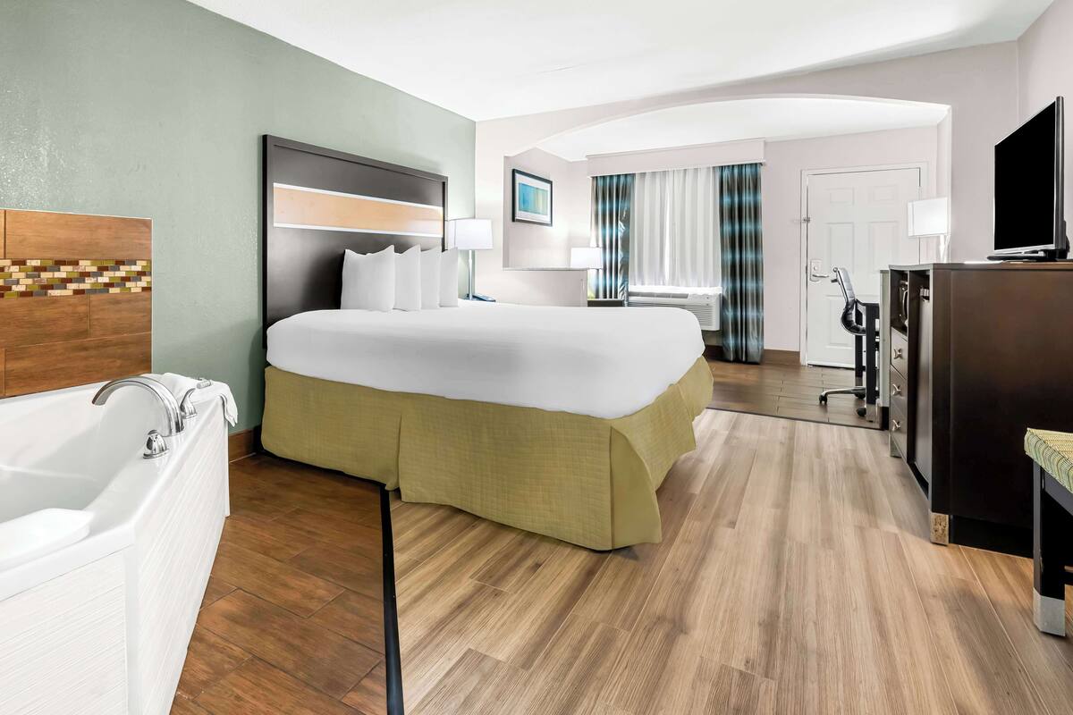 A hotel room with a large bed, a separate bathroom with a bathtub, a desk with a chair, and a television.