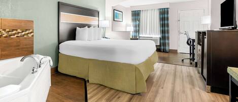 A hotel room with a large bed, a separate bathroom with a bathtub, a desk with a chair, and a television.