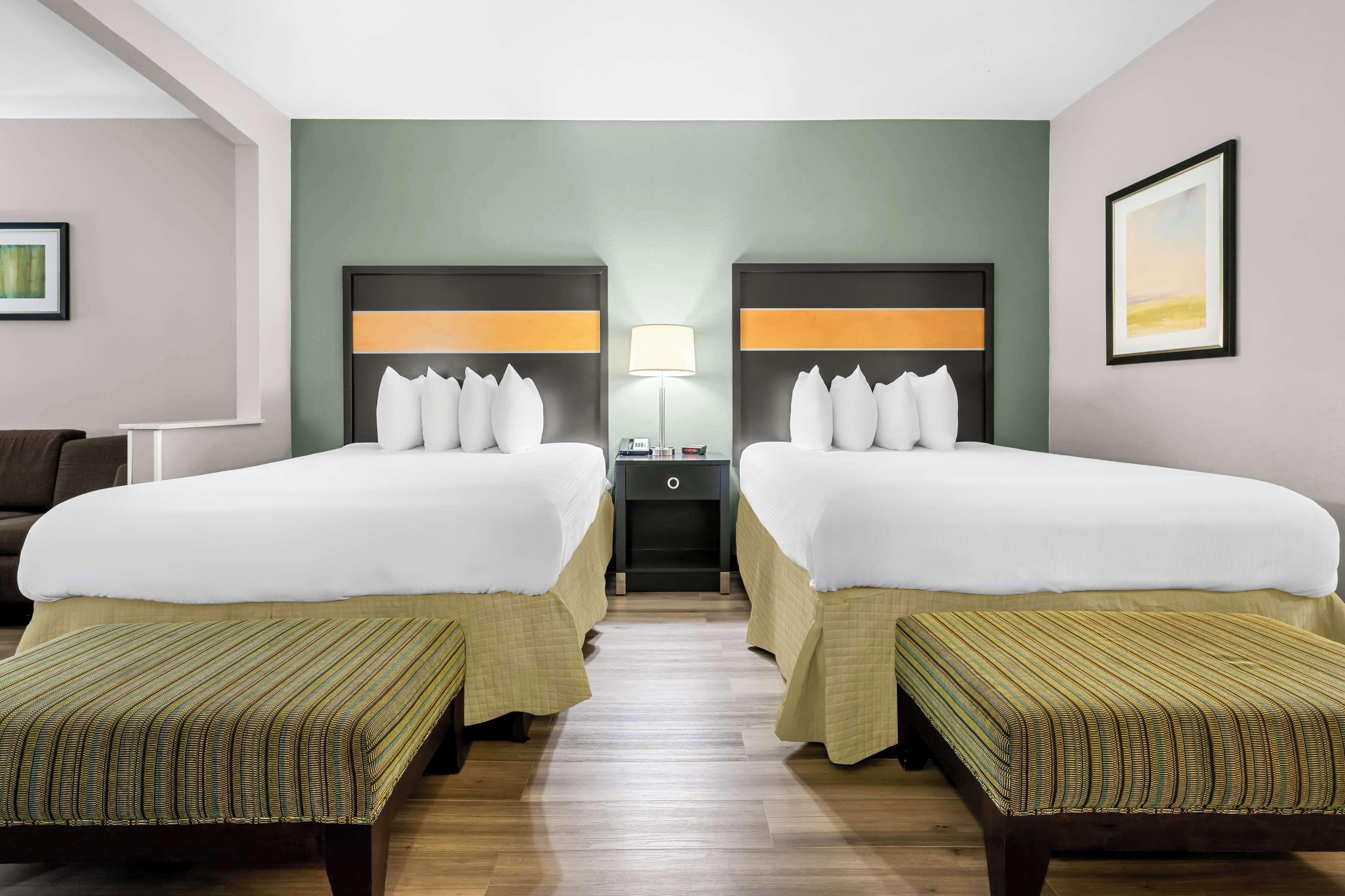 Habitació d'hotel amb dos llits, una tauleta de nit, una làmpada i una banca.