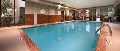 An indoor swimming pool with clear water, surrounded by a tiled deck and a brick border.