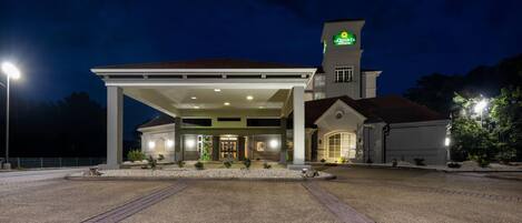 A hotel with a covered outdoor area, a tower with a sign, and a well-lit entrance.