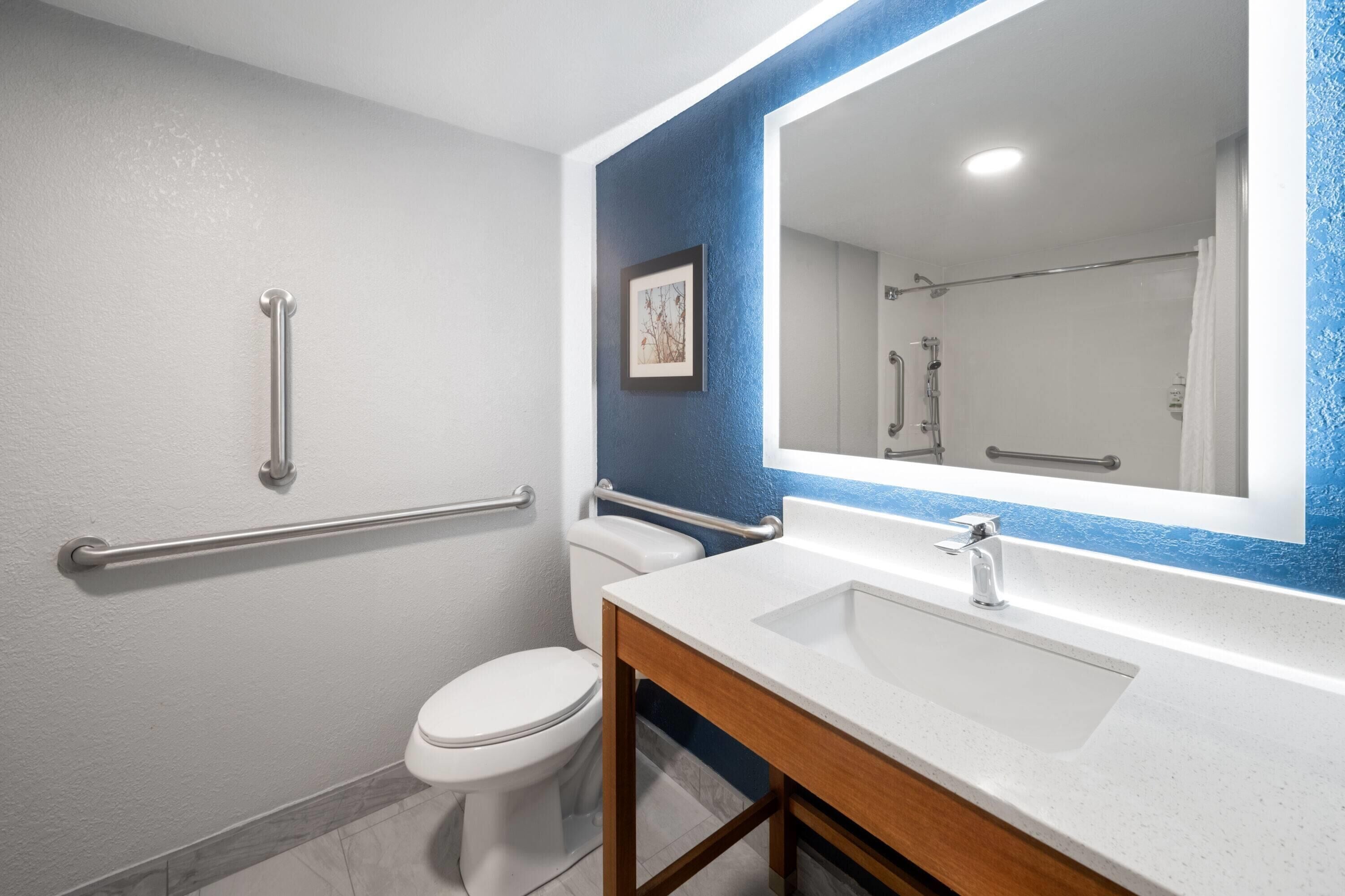A bathroom with a white toilet, a sink with a large mirror, and a blue accent wall.