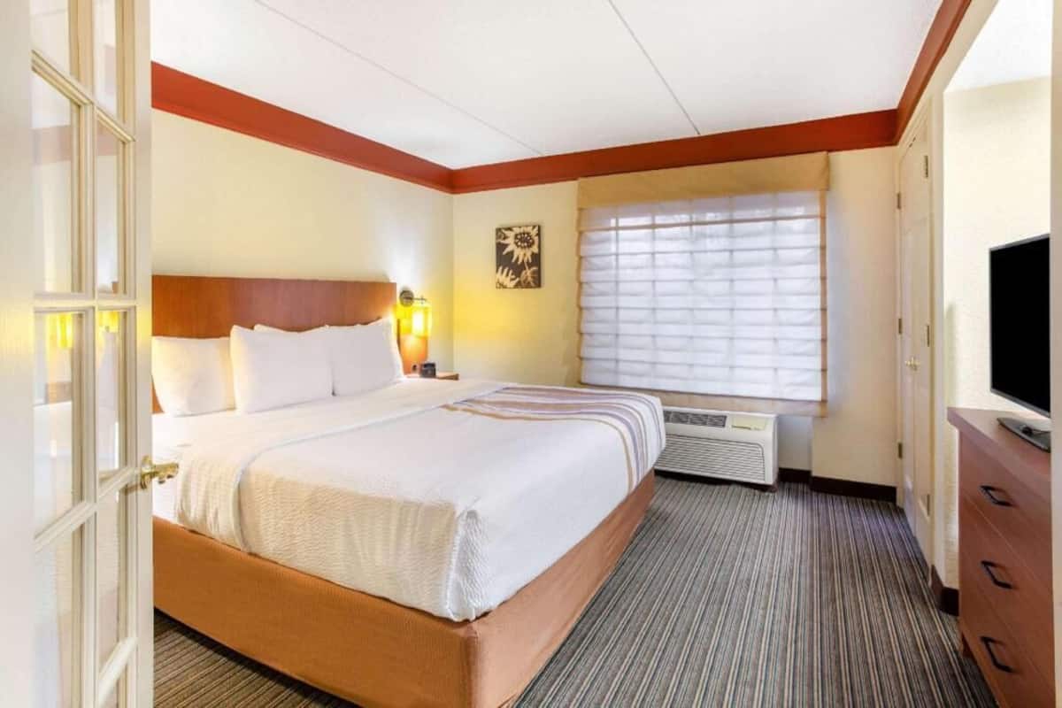 A hotel room with a bed, a TV, a heater, and a window with blinds.
