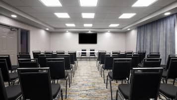 A conference room with rows of chairs, a large screen, and a carpeted floor.