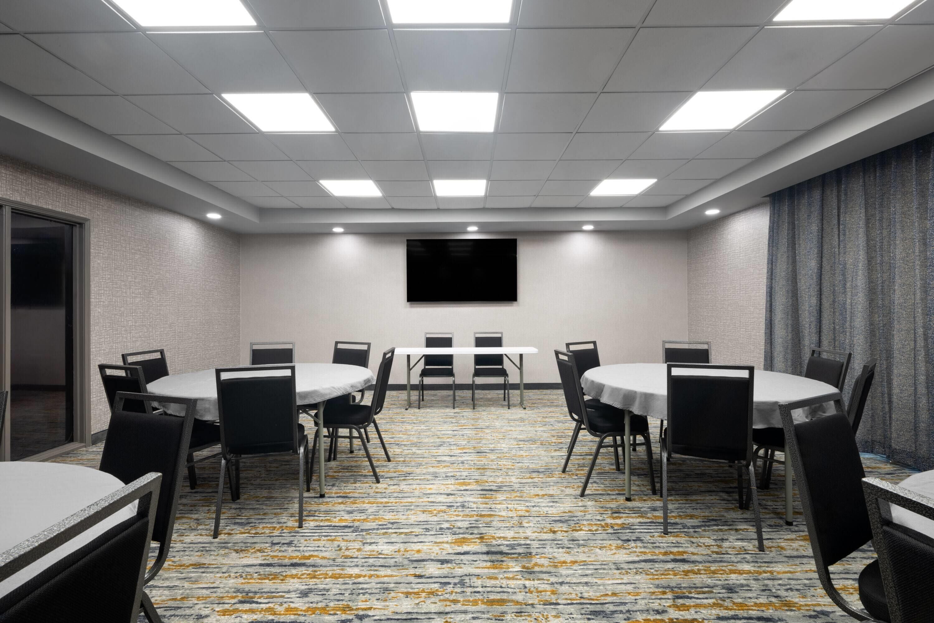 A conference room with a carpeted floor, round tables, and chairs.