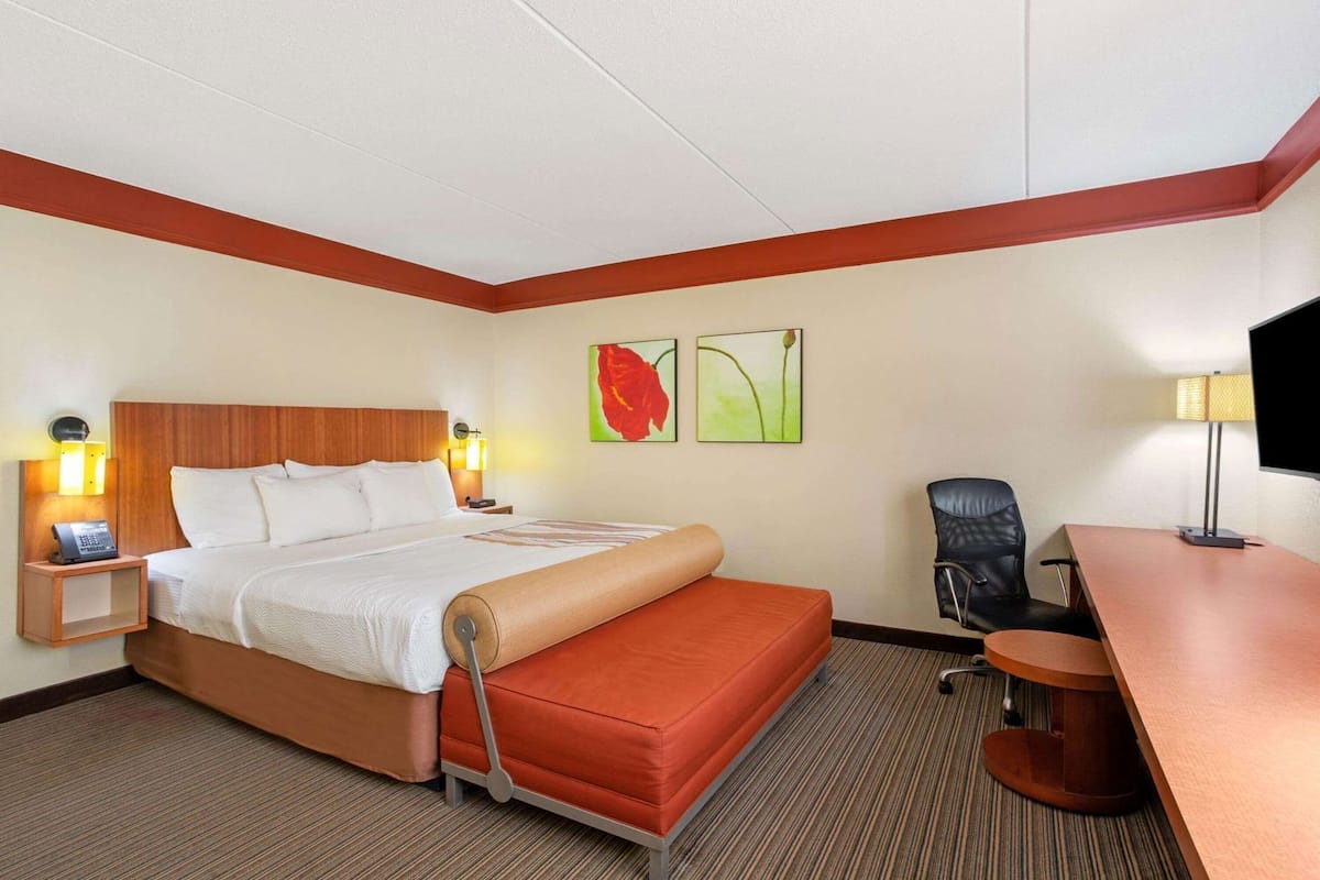 A hotel room with a bed, a desk, a chair, a telephone, and two wall-mounted lamps.