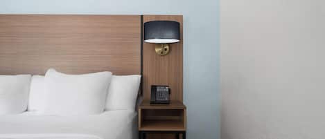 Una cama bien hecha con sábanas blancas, una mesita de noche de madera con una lámpara y un teléfono.