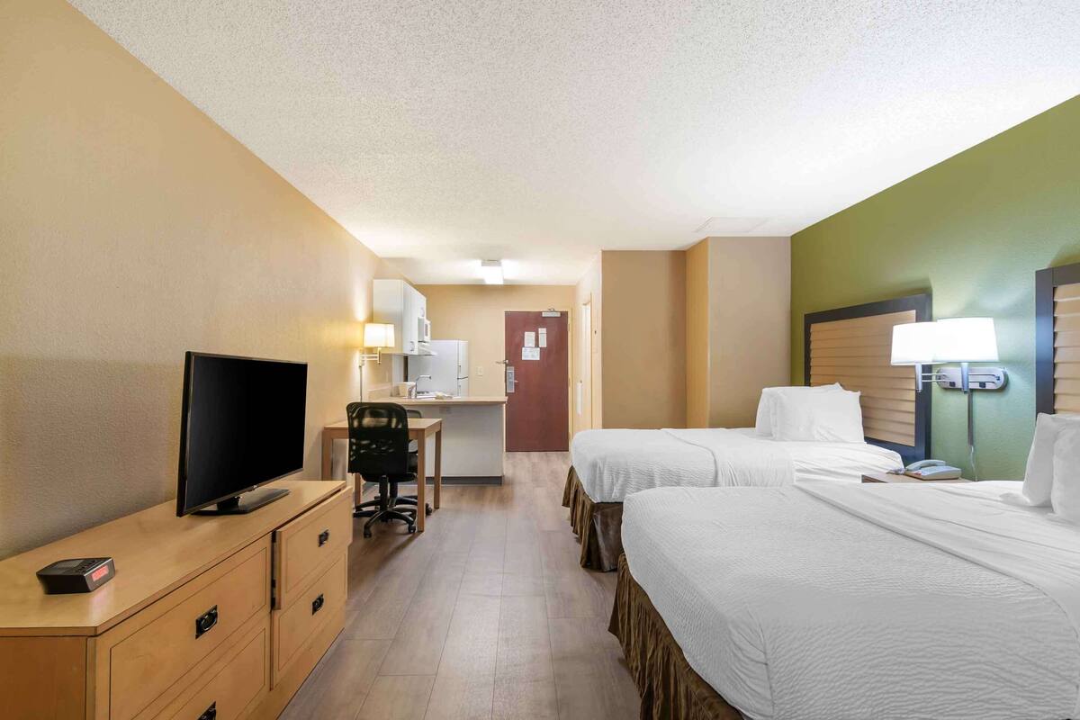 A hotel room with two beds, a desk with a computer, a TV, and a lamp.
