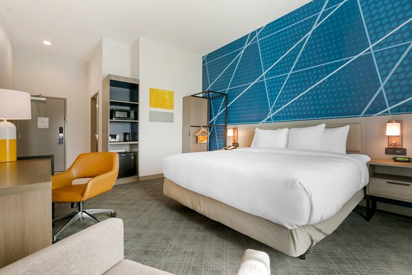 A hotel room with a large bed, a desk with a chair, a wardrobe, and a blue patterned wall.