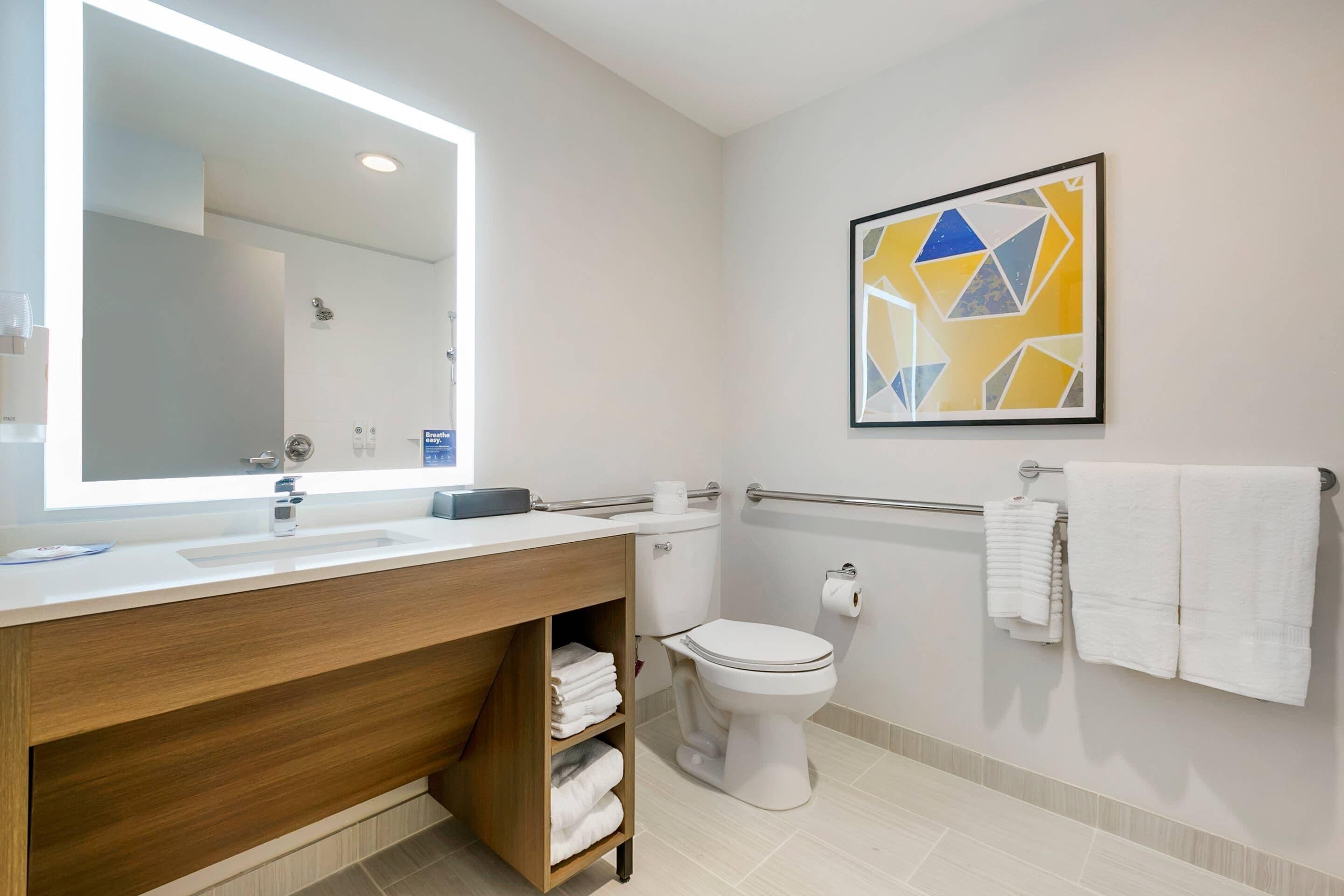 Uma casa de banho moderna com um espelho grande, loiça branca, sanita e um porta-toalhas.