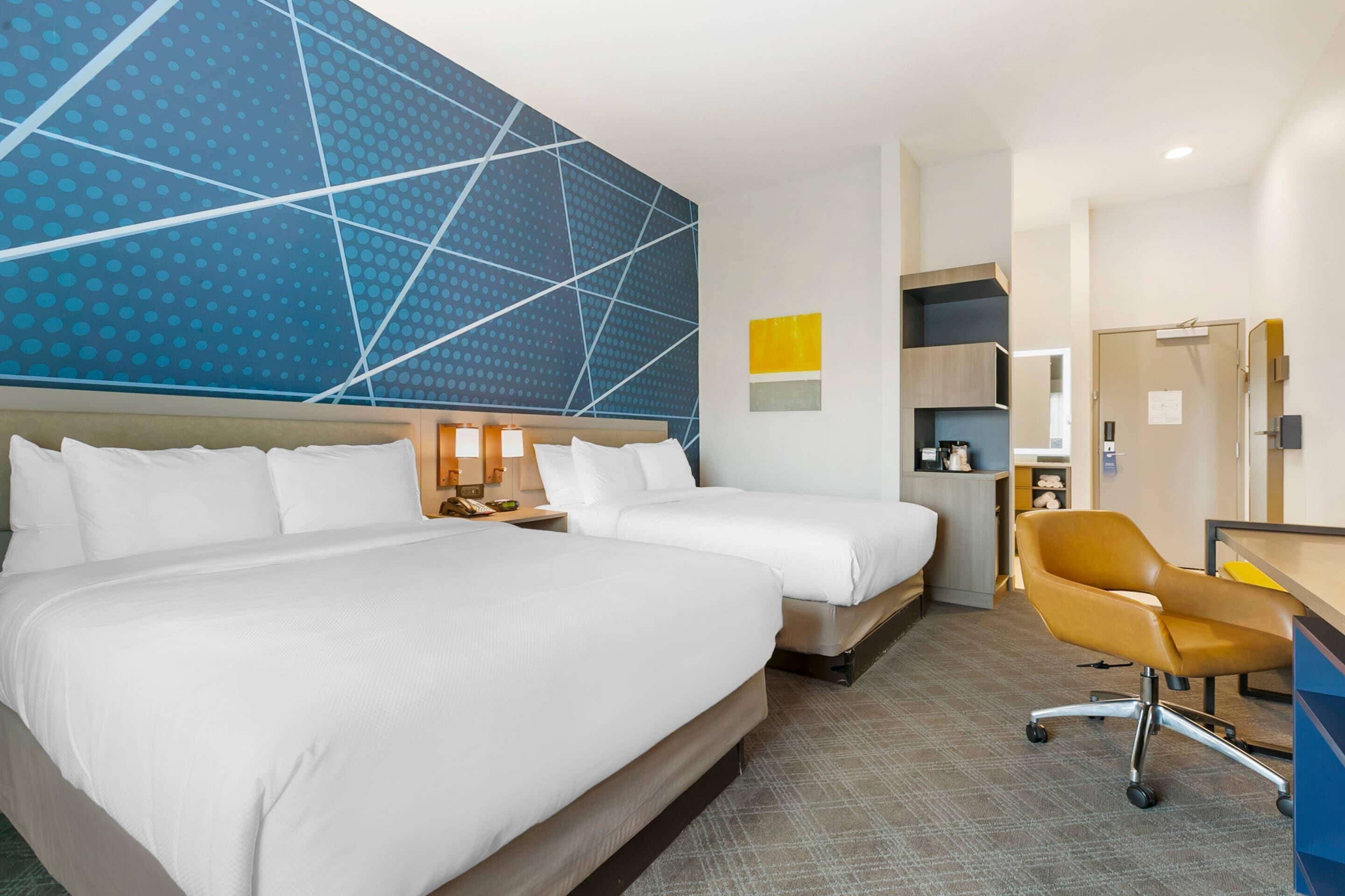Ein Hotelzimmer mit zwei Betten, einem Schreibtisch, einem Stuhl und einer Wand mit großem geometrischem Muster.