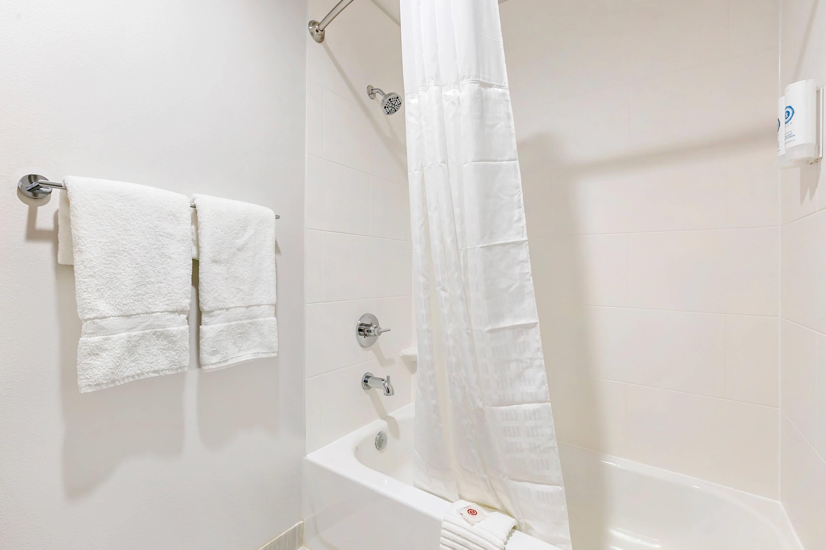 A bathroom with a bathtub, a shower curtain, and two towels hanging on a wall.