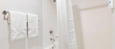A bathroom with a bathtub, a shower curtain, and two towels hanging on a wall.