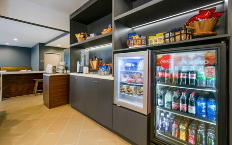 A modern kitchen with a refrigerator stocked with beverages, a coffee machine, and a variety of snacks.