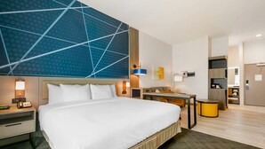 Une chambre d’hôtel moderne équipée d’un grand lit, de tables de chevet, d’un bureau et d’une kitchenette.