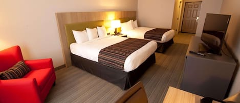 Una habitación de hotel con dos camas, un sillón rojo, un escritorio con una computadora y un televisor.