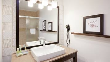 A bathroom with a large mirror, a white sink, a towel rack, and a framed picture on the wall.