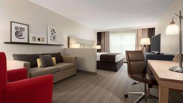 A hotel room with a sofa, a red armchair, a desk, a bed, and a television.