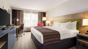A hotel room with a large bed, a desk with a computer, a chair, and a TV.