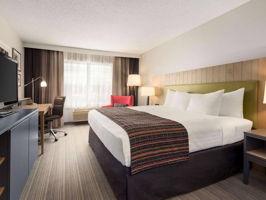 A hotel room with a large bed, a desk with a computer, a chair, and a TV.