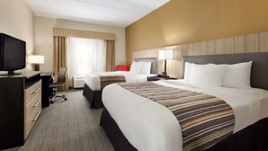 A hotel room with two beds, a desk with a television, a chair, and a window with curtains.
